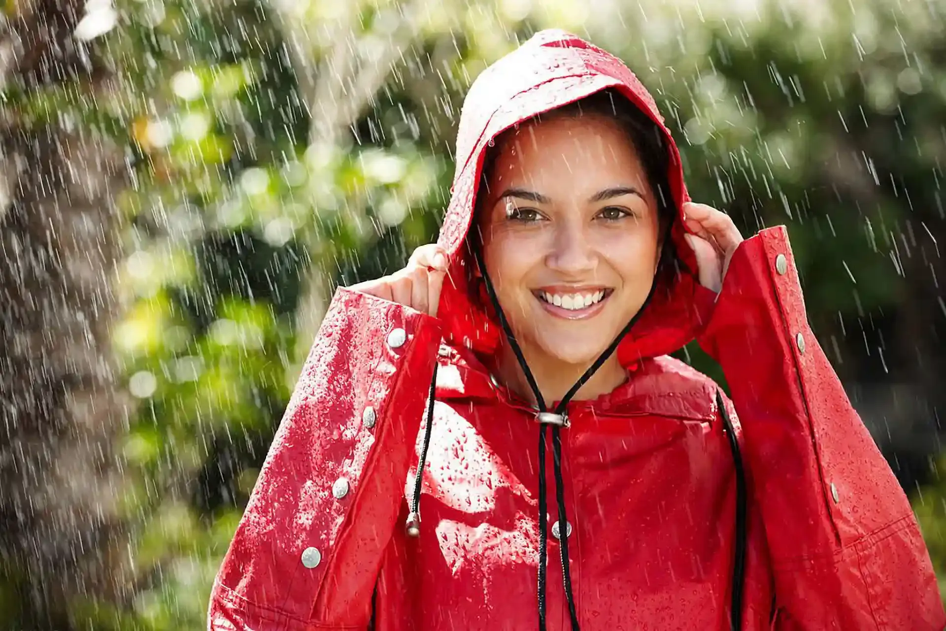 A smiling woman in a red hooded raincoat standing in the rain.