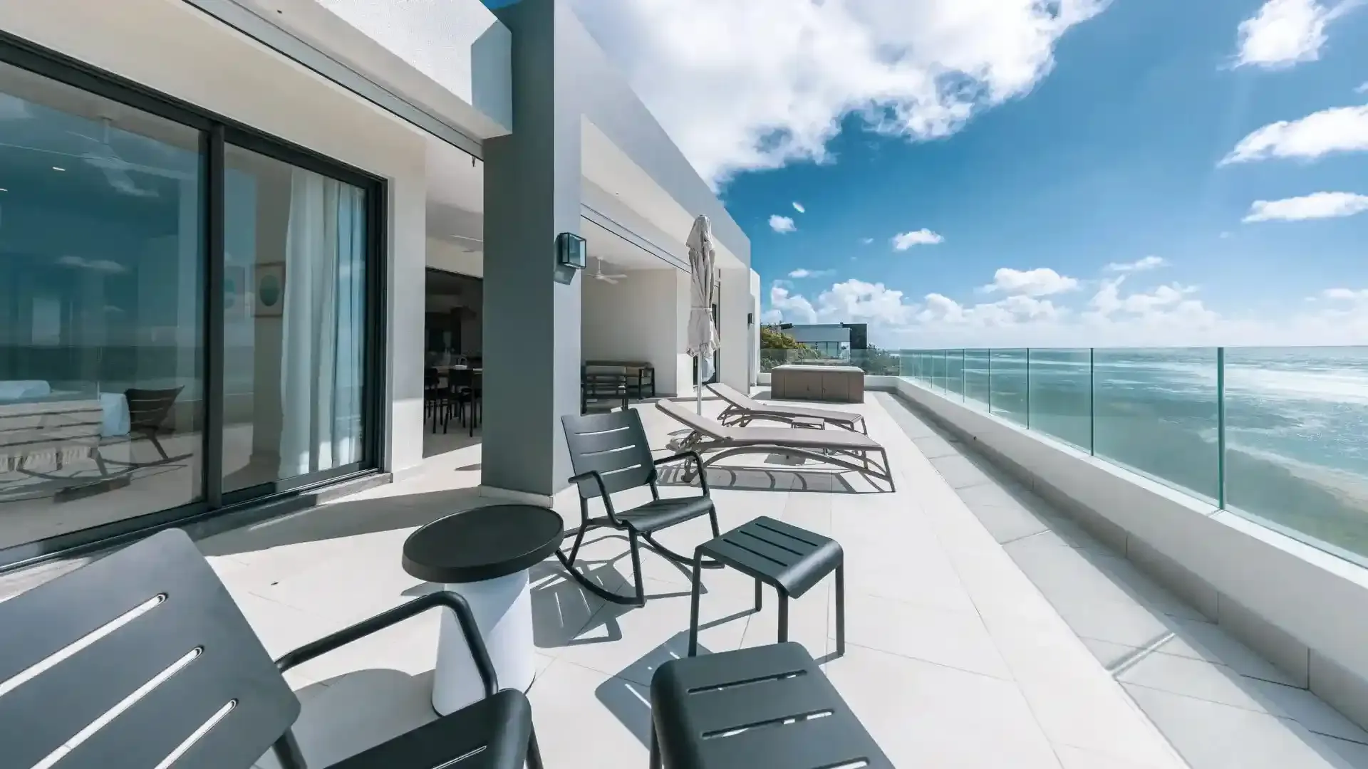 Sunlit terrace with loungers and a glass balustrade overlooking the sea.